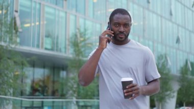 İyi sabahlar. Afrikalı bir adam dışarıda akıllı telefondan konuşmak için kahve içiyor. Elinde cep telefonu bardağı olan bir adam sokakta yürüyor. Cep telefonuyla cevap veren adam cep telefonuyla konuşuyor.