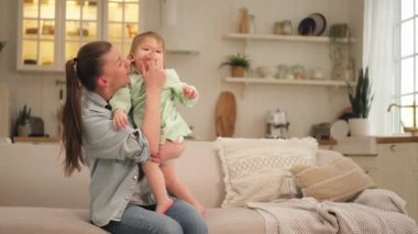 Evde mutlu bir aile. Anne ve bebek evdeki kanepede oynuyorlar. Anne bebeğe sevgiyle sarılıyor. Küçük bebek anne birlikte eğleniyor. Genç kadın anne, küçük kız oturma odasında dinleniyor.