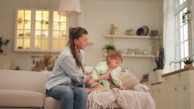 Evde mutlu bir aile. Anne kucağında küçük bir kız çocuğu taşıyor. Anne ve küçük kız evde birlikte eğleniyorlar. Anne bebeğe sevgiyle sarılır. Genç anne çocuk oturma odasında dinleniyor.