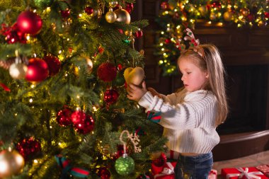 Mutlu Noeller Noel tatili. Noel arifesinde evde Noel ağacı süsleyen küçük bir kız. Klasik Noel ağacının yanında, elinde kış süsleri olan genç bir çocuk. Noel 'i kutlama zamanı.