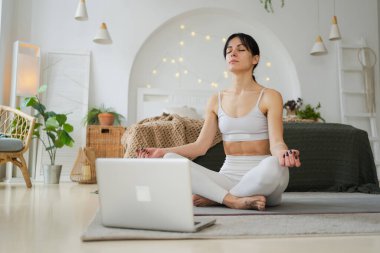 Yoga farkındalığı meditasyonu çevrimiçi. Evde dizüstü bilgisayar dersleriyle yoga yapan bir kadın. Lotus 'ta oturan kadın içeride meditasyon yapıyor. Nefes egzersizi yapan bir kız. Evde yoga.