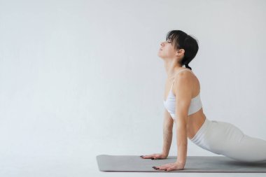 Yoga fitness antrenmanı. Beyaz arka planda yoga yapan bir kadın. Yoga minderinde spor yapan bir kadın. Spor giyim bölümündeki kız kilo vermek için antrenman yapıyor. Spor ve zindelik