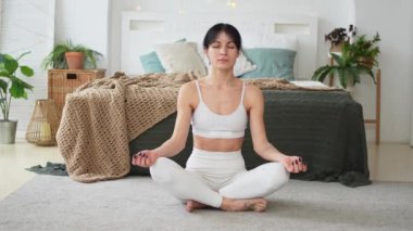 Yoga farkındalığı meditasyonu. Sağlıklı bir kadın evdeki oturma odasında yoga yapıyor. Lotus 'ta oturan kadın meditasyon yapıyor, gülümsüyor, evde dinleniyor. Nefes egzersizi yapan bir kız. Evde yoga.