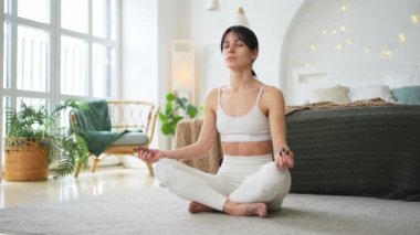 Yoga farkındalığı meditasyonu. Sağlıklı bir kadın evdeki oturma odasında yoga yapıyor. Lotus 'ta oturan kadın meditasyon yapıyor, gülümsüyor, evde dinleniyor. Nefes egzersizi yapan bir kız. Evde yoga.