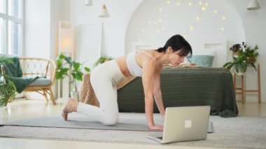 Yoga fitness antrenmanı online. Evde dizüstü bilgisayar dersleriyle yoga yapan bir kadın. Yoga minderinde spor yapan bir kadın. Kız kilo vermek için antrenman yapıyor. Spor uygunluğu