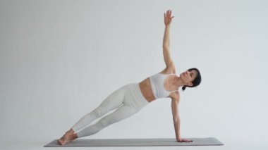 Yoga fitness antrenmanı. Beyaz arka planda yoga yapan bir kadın. Yoga minderinde spor yapan bir kadın. Spor giyim bölümündeki kız kilo vermek için antrenman yapıyor. Spor ve zindelik