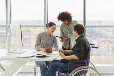 Takım çalışması beyin fırtınası. Çeşitli çok ırklı meslektaşlar birlikte çalışan engelli insanlar için sandalyede oturuyor. Yaratıcı ofiste oturup iş konuşan bir grup insan. Genç profesyonel takım