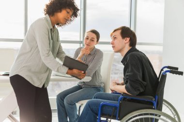 Takım çalışması beyin fırtınası. Çeşitli çok ırklı meslektaşlar birlikte çalışan engelli insanlar için sandalyede oturuyor. Yaratıcı ofiste oturup iş konuşan bir grup insan. Genç profesyonel takım