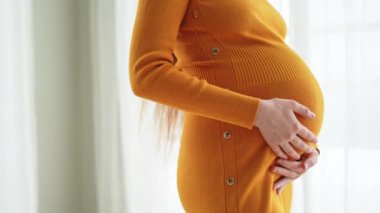 Hamilelik anneliği insanların gelecek beklentisi. Hamile kadın elleri pencerenin yanındaki koca göbeğe dokunuyor. Karnına sarılan ve hamileliğin tadını çıkaran bir kız. Annelik şefkati ebeveynlik yeni yaşam konsepti