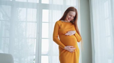 Hamilelik anneliği insanların gelecek beklentisi. Evinin penceresinin yanında koca göbekli hamile bir kadın var. Karnına sarılan ve hamileliğin tadını çıkaran bir kız. Annelik şefkati ebeveynlik yeni yaşam konsepti