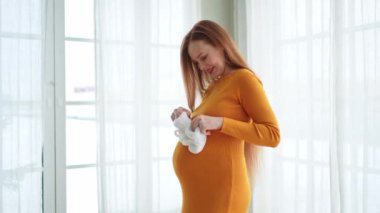 Hamilelik anneliği insanların gelecek beklentisi. Koca göbekli hamile bir kadın kucağında bebek poposu ile evde gülümsüyor. Genç anne hamileliğin tadını çıkarıyor. Annelik şefkati ebeveynlik yeni bir hayat