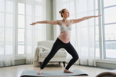 Hamilelik yoga antrenmanı. Hamile kadın evde yoga yapıyor. Hamile kız içeride yoga minderiyle spor yapıyor. Koca göbekli bir kadın Asya antrenmanı yapıyor.