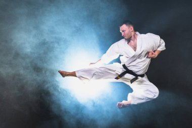 Siyah kuşak atlamalı, beyaz kimonolu, karate dövüş sanatları için güçlü bir dövüşçü. Adam eğitimi gölge dövüşü alıştırması yapıyor dövüş antrenmanlarına hazırlanıyor antrenmanlara hazır