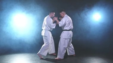 Karanlık arka planda dövüş sanatları ustaları. Siyah spor salonunda karate dövüş sporları eğitimi için beyaz kimonolu güçlü dövüşçüler. Karate dövüşçüleri antrenman yapıyor. Dövüş antrenmanı yapıyor.