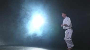 Siyah kuşak atlamalı, beyaz kimonolu, karate dövüş sanatları için güçlü bir dövüşçü. Adam eğitimi gölge dövüşü alıştırması yapıyor dövüş antrenmanlarına hazırlanıyor antrenmanlara hazır