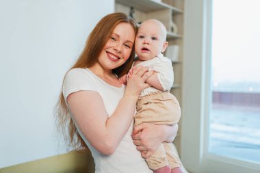 Evde mutlu bir aile. Anne kucağında küçük bir kız çocuğu. Anne ve bebek evde birlikte oynayarak rahatlar. Anne bebeğe sevgiyle sarılır. Bebeği emziren anne.