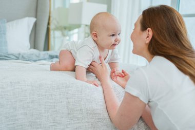 Evde mutlu bir aile. Anne, küçük bebekle yatakta oynuyor. Anne bebek birlikte oynayıp rahatlıyor. Anne bebeğe sevgiyle bakar. Bebeği emziren anne oturma odasında dinleniyor.