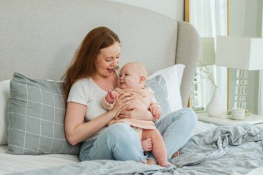 Evde mutlu bir aile. Anne, küçük bebekle yatakta oynuyor. Anne bebek birlikte oynayıp rahatlıyor. Anne bebeğe sevgiyle bakar. Bebeği emziren anne oturma odasında dinleniyor.