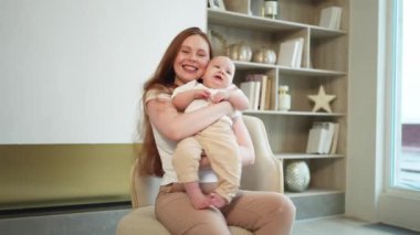 Evde mutlu bir aile. Anne kucağında küçük bir kız çocuğu. Anne ve bebek evde birlikte oynayarak rahatlar. Anne bebeğe sevgiyle sarılır. Bebeği emziren anne.