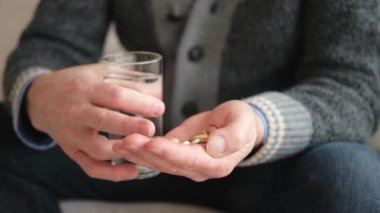 Haplı eller. Yaşlı adam ellerinde tıbbi hap ve bir bardak su tutuyor. Olgun yaşlı büyükbaba ilaç tedavisi hapları alıyor vitamin. Yaş reçeteli ilaç sağlık tedavisi kavramı