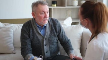 Doktor muayenehanesinde ya da evde yaşlı bir adamı muayene eden kadın doktor. Yaşlı hasta ve doktorun hastane odasında muayeneleri var. Tıbbi sağlık hizmetleri sağlık kontrolü. Doktoru ziyaret et.