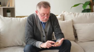 Evdeki kanepede oturan orta yaşlı bir adam elinde tıbbi haplar tutuyor. Yaşlı büyükbaba ilaç tedavisi hapı vitamini alıyor. Yaş reçeteli ilaç sağlık tedavisi kavramı