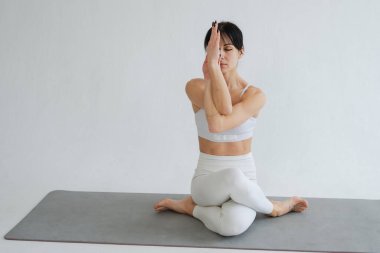 Yoga fitness antrenmanı. Beyaz arka planda yoga yapan bir kadın. Yoga minderinde spor yapan bir kadın. Spor giyim bölümündeki kız kilo vermek için antrenman yapıyor. Spor ve zindelik