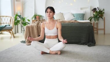 Yoga farkındalığı meditasyonu. Sağlıklı bir kadın evdeki oturma odasında yoga yapıyor. Lotus 'ta oturan kadın meditasyon yapıyor, gülümsüyor, evde dinleniyor. Nefes egzersizi yapan bir kız. Evde yoga.