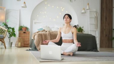 Yoga farkındalığı meditasyonu çevrimiçi. Evde dizüstü bilgisayar dersleriyle yoga yapan bir kadın. Lotus 'ta oturan kadın içeride meditasyon yapıyor. Nefes egzersizi yapan bir kız. Evde yoga.