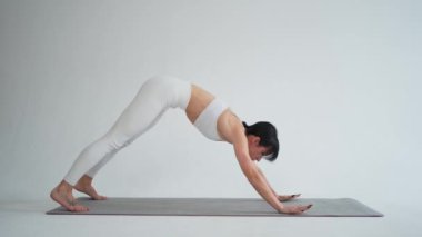 Yoga fitness antrenmanı. Beyaz arka planda yoga yapan bir kadın. Yoga minderinde spor yapan bir kadın. Spor giyim bölümündeki kız kilo vermek için antrenman yapıyor. Spor ve zindelik