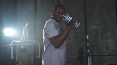 Beden eğitiminde spor. Spor salonunda dambılları toplayan Afrikalı Amerikalı bir vücut geliştirici. Fitness kulübünde halterli kasları çalıştırmak için ağırlık çalışıyorum. Spor yapan bir adam. Sağlıklı yaşam tarzı