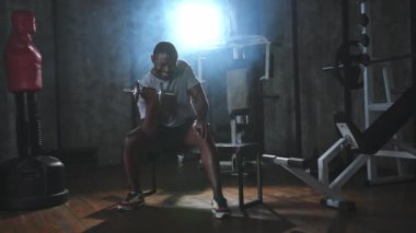 Beden eğitiminde spor. Spor salonunda dambılları toplayan Afrikalı Amerikalı bir vücut geliştirici. Fitness kulübünde halterli kasları çalıştırmak için ağırlık çalışıyorum. Spor yapan bir adam. Sağlıklı yaşam tarzı