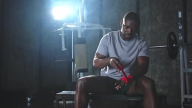 Beden eğitiminde spor. Afrikalı Amerikalı boksör elleri kırmızı boksla sarmalamaya hazırlanıyor spor amaçlı bandajlar spor salonunda. Güçlü adam boks antrenmanına hazır.