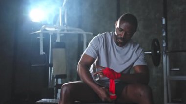 Beden eğitiminde spor. Afrikalı Amerikalı boksör elleri kırmızı boksla sarmalamaya hazırlanıyor spor amaçlı bandajlar spor salonunda. Güçlü adam boks antrenmanına hazır.