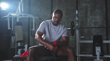 Beden eğitiminde spor. Afrikalı Amerikalı boksör elleri kırmızı boksla sarmalamaya hazırlanıyor spor amaçlı bandajlar spor salonunda. Güçlü adam boks antrenmanına hazır.