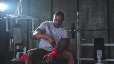 Beden eğitiminde spor. Afrikalı Amerikalı boksör elleri kırmızı boksla sarmalamaya hazırlanıyor spor amaçlı bandajlar spor salonunda. Güçlü adam boks antrenmanına hazır.