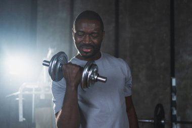 Beden eğitiminde spor. Spor salonunda dambılları toplayan Afrikalı Amerikalı bir vücut geliştirici. Fitness kulübünde halterli kasları çalıştırmak için ağırlık çalışıyorum. Spor yapan bir adam. Sağlıklı yaşam tarzı