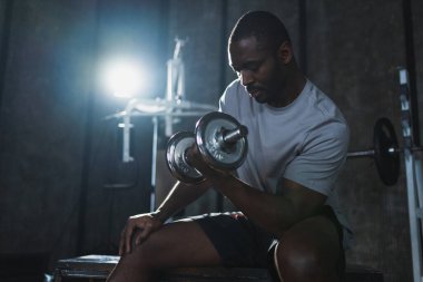 Beden eğitiminde spor. Spor salonunda dambılları toplayan Afrikalı Amerikalı bir vücut geliştirici. Fitness kulübünde halterli kasları çalıştırmak için ağırlık çalışıyorum. Spor yapan bir adam. Sağlıklı yaşam tarzı