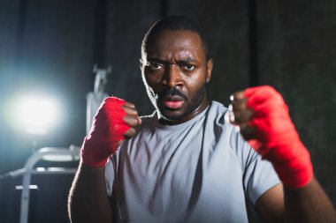 Spor salonunda boksör. Saldırgan Afrikalı dövüşçü boks eğitiminden sonra dinleniyor kameraya bakarak dövüşmeye hazır. Güçlü terli adam yumruklarını eğitiyor. Doğruca antrenmana hazırlanıyor.