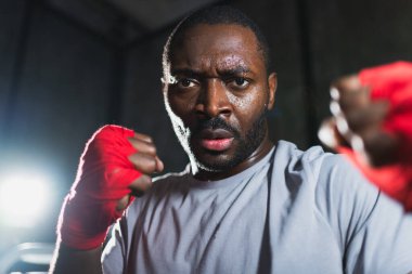 Spor salonunda boksör. Saldırgan Afrikalı dövüşçü boks eğitiminden sonra dinleniyor kameraya bakarak dövüşmeye hazır. Güçlü terli adam yumruklarını eğitiyor. Doğruca antrenmana hazırlanıyor.