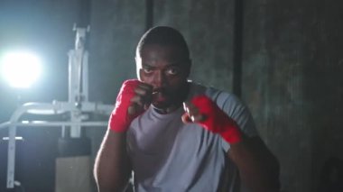 Beden eğitiminde. Afrikalı dövüşçü boksörlere yumruk atmaya hazır koruyucu bandajları kameraya sarar. Güçlü bir adam boks antrenmanına hazırlanıyor.