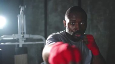 Beden eğitiminde. Afrikalı dövüşçü boksörlere yumruk atmaya hazır koruyucu bandajları kameraya sarar. Güçlü bir adam boks antrenmanına hazırlanıyor.