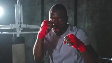 Beden eğitiminde. Afrikalı dövüşçü boksörlere yumruk atmaya hazır koruyucu bandajları kameraya sarar. Güçlü bir adam boks antrenmanına hazırlanıyor.