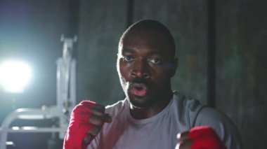 Spor salonunda boksör. Saldırgan Afrikalı dövüşçü boks eğitiminden sonra dinleniyor kameraya bakarak dövüşmeye hazır. Güçlü terli adam yumruklarını eğitiyor. Doğruca antrenmana hazırlanıyor.