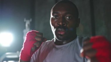 Spor salonunda boksör. Saldırgan Afrikalı dövüşçü boks eğitiminden sonra dinleniyor kameraya bakarak dövüşmeye hazır. Güçlü terli adam yumruklarını eğitiyor. Doğruca antrenmana hazırlanıyor.
