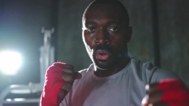 Spor salonunda boksör. Saldırgan Afrikalı dövüşçü boks eğitiminden sonra dinleniyor kameraya bakarak dövüşmeye hazır. Güçlü terli adam yumruklarını eğitiyor. Doğruca antrenmana hazırlanıyor.