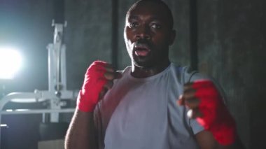 Spor salonunda boksör. Saldırgan Afrikalı dövüşçü boks eğitiminden sonra dinleniyor kameraya bakarak dövüşmeye hazır. Güçlü terli adam yumruklarını eğitiyor. Doğruca antrenmana hazırlanıyor.