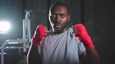 Spor salonunda boksör. Saldırgan Afrikalı dövüşçü boks eğitiminden sonra dinleniyor kameraya bakarak dövüşmeye hazır. Güçlü terli adam yumruklarını eğitiyor. Doğruca antrenmana hazırlanıyor.