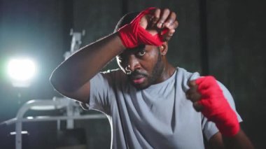 Spor salonunda boksör. Kırmızı boks ambalajlı yorgun Afrikalı boksör spor salonundaki boks antrenmanından sonra ter temizliyor. Boks müsabakasından sonra güçlü, terli bir sporcu. Spor salonunda antrenman günü