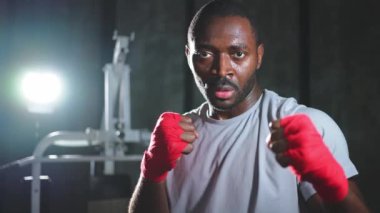Spor salonunda boksör. Saldırgan Afrikalı dövüşçü boks eğitiminden sonra dinleniyor kameraya bakarak dövüşmeye hazır. Güçlü terli adam yumruklarını eğitiyor. Doğruca antrenmana hazırlanıyor.